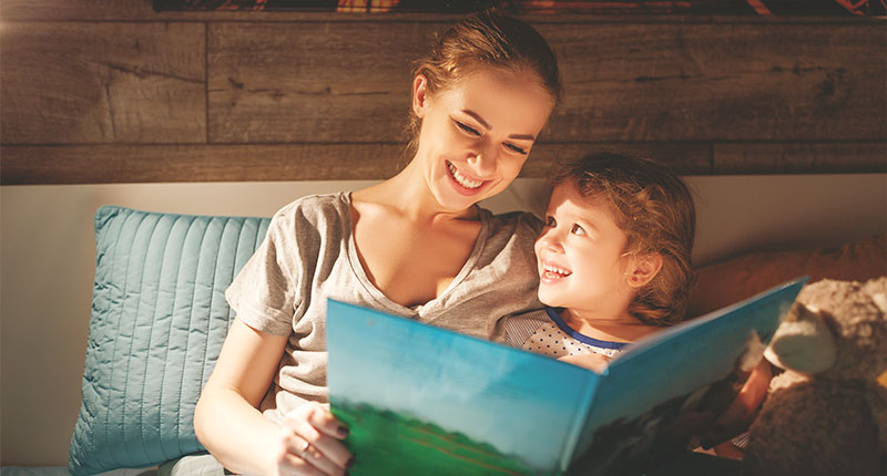 Mamma che legge un libro alla figla abbracciati nel letto