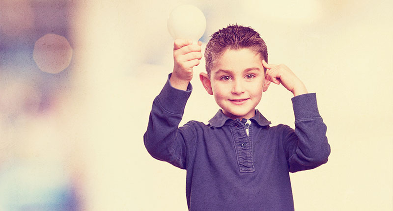 bambino con una finta lampadina in mano che mostra di avere avuto un'idea